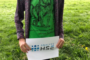 Kind mit grünem T-Shirt hält ein Schild mit dem Logo der Analyze HSE GmbH – Sponsoring beim Regenwald-Spendenlauf 2023.