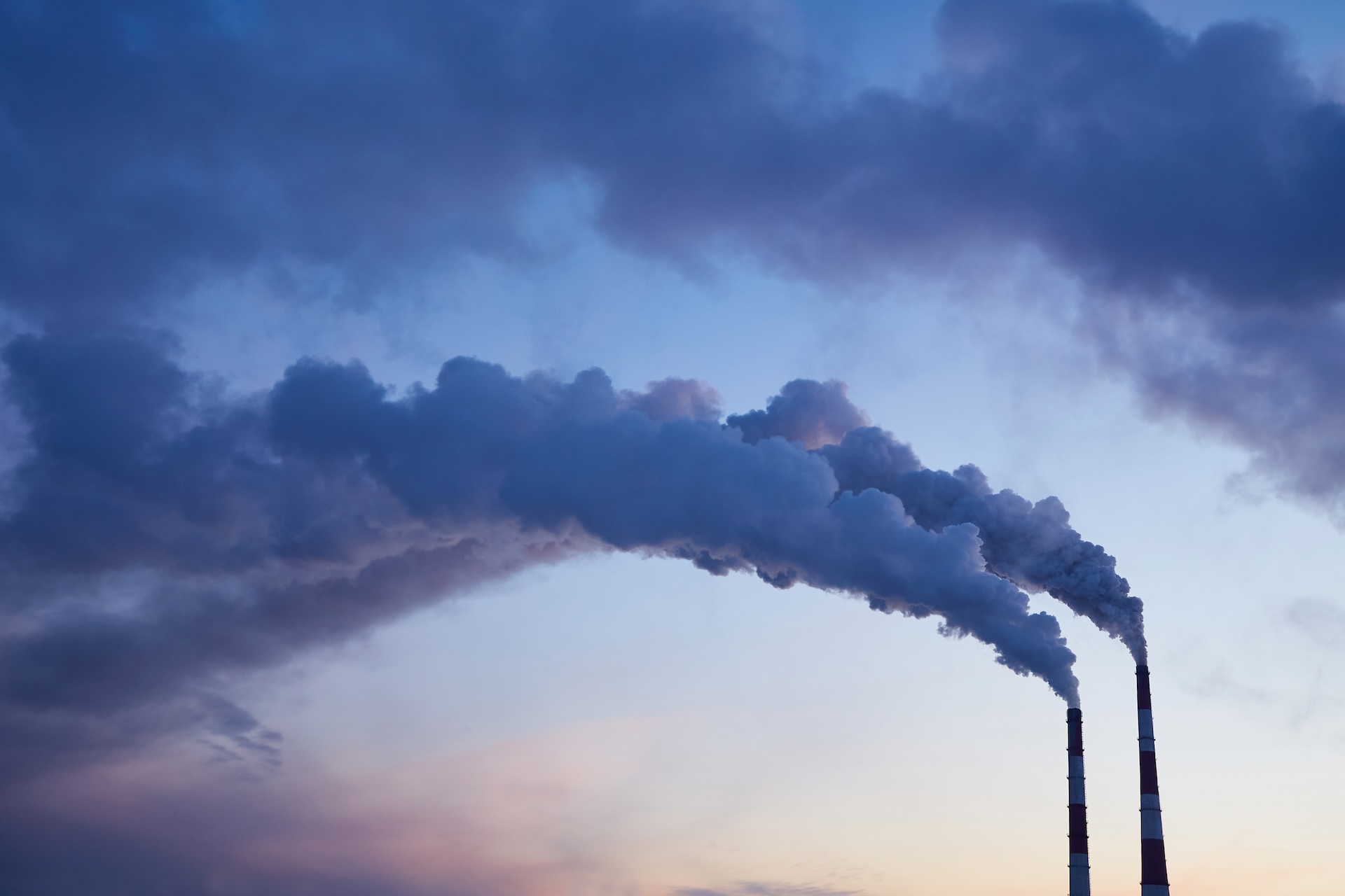 Industrielle Schornsteine mit Rauchwolken als Symbol für Emissionen in der Treibhausgasbilanzierung von Analyze HSE GmbH